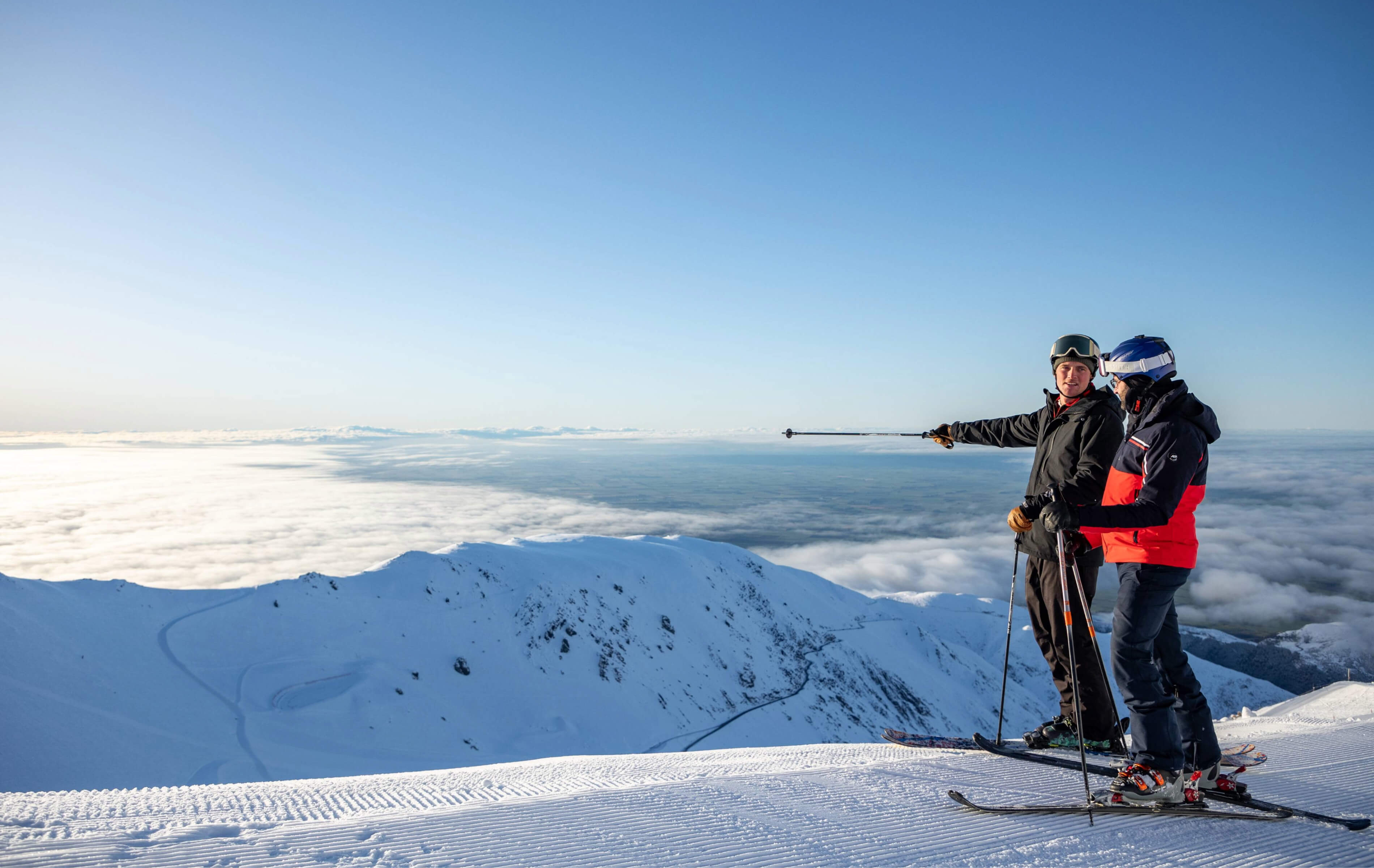 Skiers on a snowy mountain peak above a sea of clouds at Mt Hutt